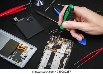 Repairing smartphone with the screw-driver on a black table. Repairman workplace. Broken cell phone diagnostics at service center.