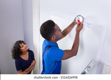 Repairman Changing Battery In Smoke Detector On Wall At Home