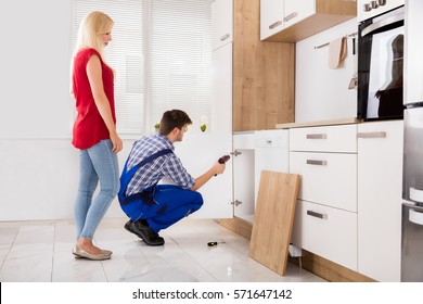 Repairman Fixing The Door Of The Kitchen Sink In Front Of Young Woman