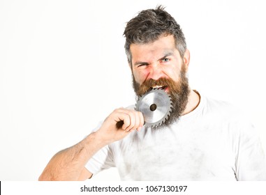 Repairman, Foreman Holds Circular Saw Blade And Bites. Strong Teeth Concept. Guy Covered With Dust. Man With Beard And Mustache On Serious Face Bites Sharp Blade, White Background.