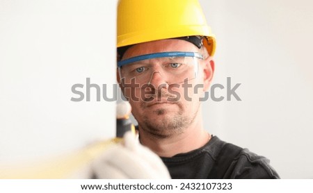 Repairman in helmet and mask, measures tape measure. Taking measurements using retractable tape. Preliminary calculations for purchase building materials. Measurements for design preparation
