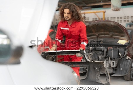 Repairman mechanic matching automobile body front bumper and assembly on damaged car at auto repair service station. Long hair man fixing vehicle bumper broken from collision crash accident on road.