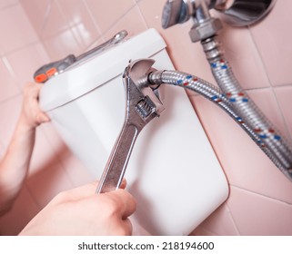 Repairman mending a toilet using a wrench