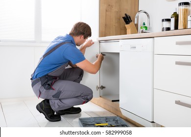 Repairman In Overalls Repairing Cabinet Hinge In Kitchen