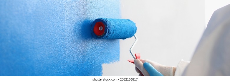 Repairman painting white wall in apartment blue using roller closeup