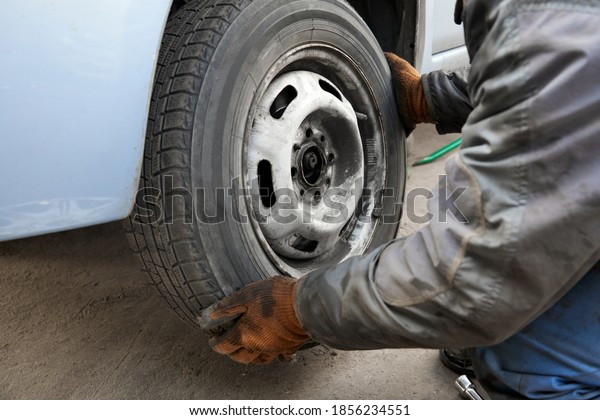 The repairman removes the wheel from\
the car for replacement. Seasonal change of car\
tires.