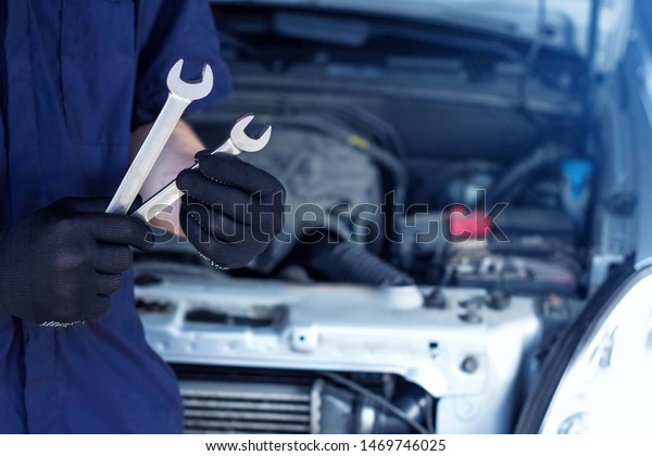 Repairman is repairing car at service station.\
Closeup mechanic hands in gloves are holding steel wrenches.\
Vehicle with open hood on background.  Modern auto repair shop with\
equipments and \
tools.