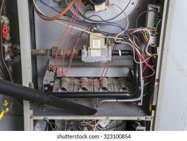 Repairman Vacuuming Inside Of A Gas Furnace During A Cleaning. 