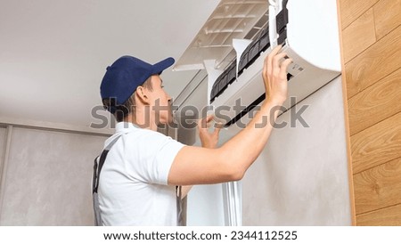 Repairman in work uniform opens air conditioner tor repair. Male worker carefully examines equipment in modern premise. Concept of service at home Stock fotó © 