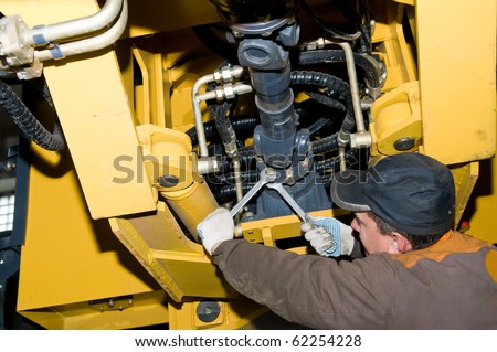 repairman worker screwing nuts of axle assembly in heavy wheel loader