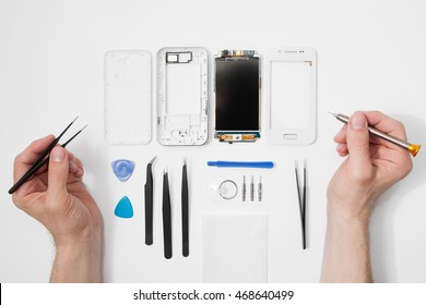 Repairman workplace with phone and special tools. Disassembled smartphone with disassembling instruments and repairer hands on white background. Electronics repair service, device production concept