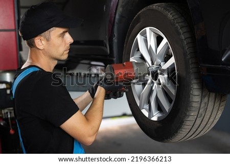 Repairman Works in a Modern Car Service. Specialists Removes the Wheel in Order to Fix a Component on a Vehicle. Mechanic is Unscrewing Lug Nuts with Pneumatic Impact Wrench.