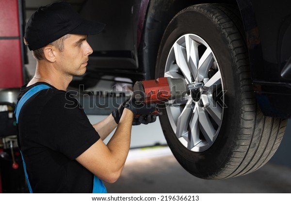 Repairman Works in a\
Modern Car Service. Specialists Removes the Wheel in Order to Fix a\
Component on a Vehicle. Mechanic is Unscrewing Lug Nuts with\
Pneumatic Impact\
Wrench.
