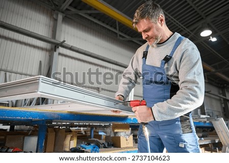 Repairman in workshop using drill to work on production of PVC windows