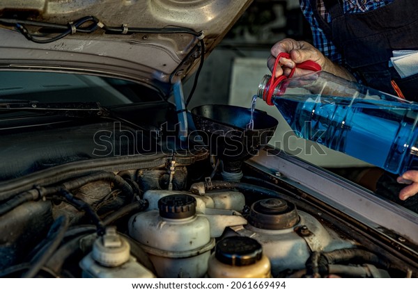 Repairman\'s male hands pouring car window washer.\
Vehicle fitter inspecting used car engine. Car components, belts,\
hoses, labor arm close up in the open hood of car. Service center,\
auto repair shop