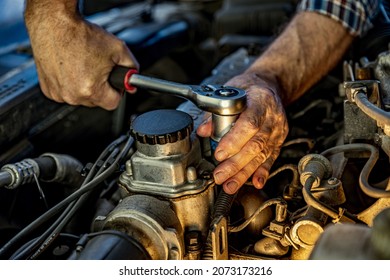 Repairman's male hands with a wrench. Vehicle fitter inspecting used car engine. Car components, belts, hoses, labor arm close up in the open hood of the car. Service center, auto repair shop