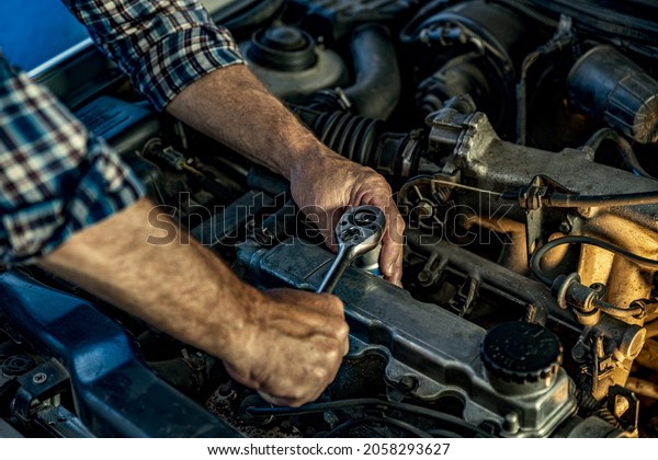 Repairman\'s male hands with a wrench. Vehicle fitter\
inspecting used car engine. Car components, belts, hoses, labor arm\
close up in the open hood of the car. Service center, auto repair\
shop