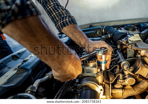Repairman's male hands with a wrench. Vehicle fitter
inspecting used car engine. Car components, belts, hoses, labor arm
close up in the open hood of the car. Service center, auto repair
shop