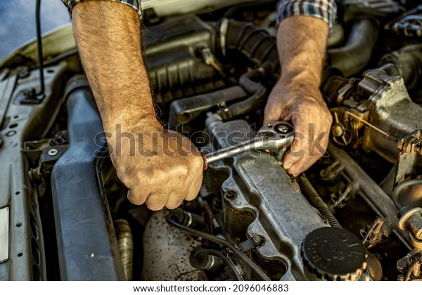 Repairman\'s male hands with a wrench. Vehicle fitter\
inspecting used car engine. Car components, belts, hoses, labor arm\
close up in the open hood of the car. Service center, auto repair\
shop