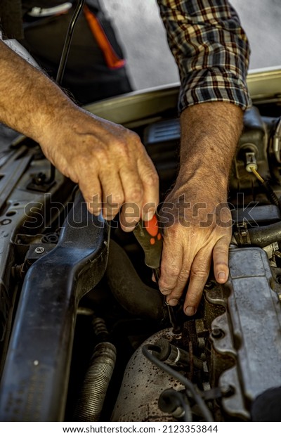 Repairman's male hands with a wrench. Vehicle fitter
inspecting used car engine. Car components, belts, hoses, labor arm
close up in the open hood of the car. Service center, auto repair
shop