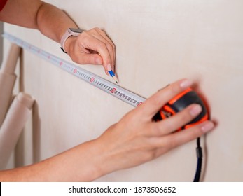 Repairs in the apartment. Close-up of a tape measure and pencil in women's hands. Measuring the walls in a room.