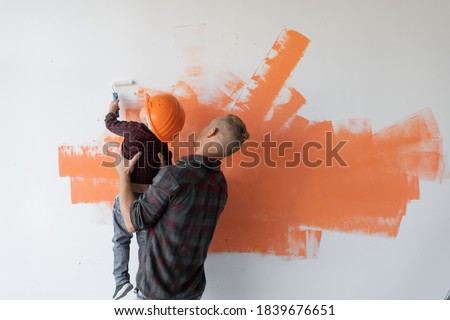 repairs his house, the father keeps his son and he helps him paint the wall with a roller,