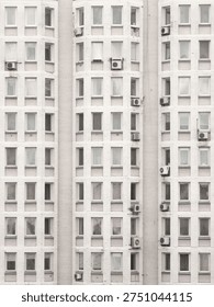 Repeating facade pattern of white brick apartment building with windows and air conditioners.