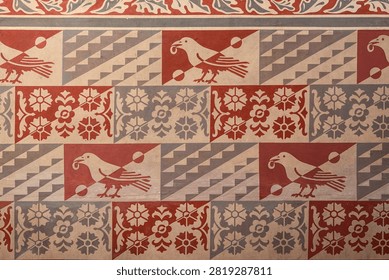 A repeating painted wall pattern shows the raven of the Corvin family, the heraldic emblem of King Matthias Corvinus, alternating with floral rosettes and geometric staircase motifs inside Matthias Church in Budapest, Hungary, with the overall composition capturing the scale and craftsmanship of the setting.