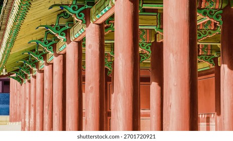 A repeating pattern of vibrant red pillars leads the eye towards intricately decorated eaves of a traditional building.