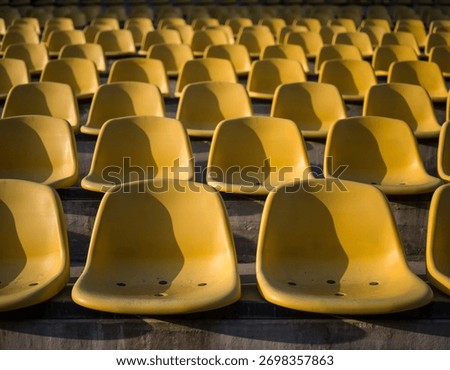 Repeating rows of empty yellow stadium seats in an outdoor sports arena at golden hour—strong shadows, geometric pattern, and symmetrical perspective creating a clean minimal architectural background 