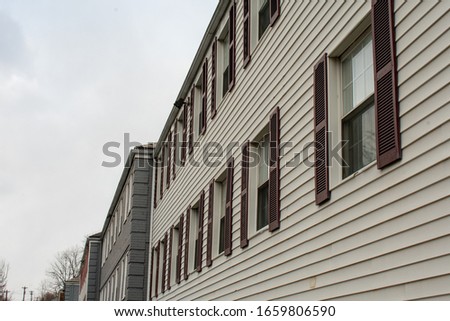 Repeating Windows With Red Shitters At an Angle With a Gray Sky in the background