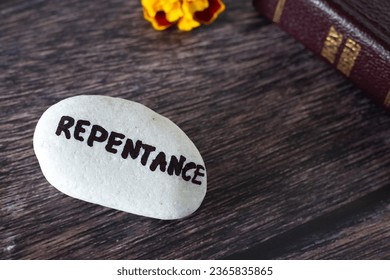 Repentance handwritten word on stone with closed holy bible book and flower on wooden background. Copy space, close-up. Confession, forgiveness, repenting of sin, Christian biblical concept.