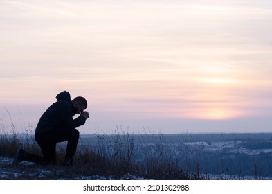 Repentance. A man on his knees. Christian, Prayer. Silhouette of a man on a blue sky background. Kneeling Prayer to God. Glorification