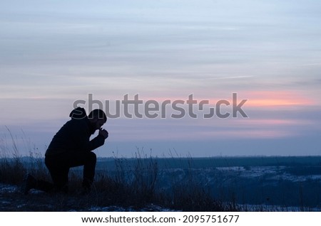 Repentance. A man on his knees. Prayer. Silhouette of a man on a blue sky background. Kneeling Prayer to God. Glorification