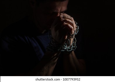 Repented Man Prisoner With His Hands Shackled In Chains On A Dark Background