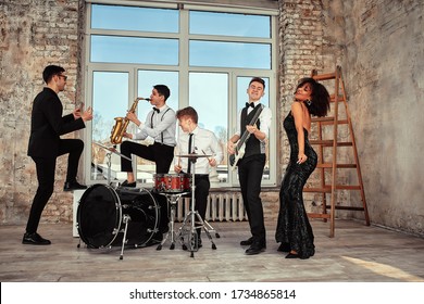 Repetition Of Multi Ethnic Jazz Band In Loft. Bass Guitar Player, Electric Guitar Player, Saxophonist And Drummer At Loft. Jazz Music And Jam Session Concept. Passion For Music And Youth Culture