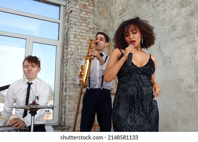 Repetition Of Multi Ethnic Jazz Band In Loft. Bass Guitar Player, Electric Guitar Player, Saxophonist And Drummer At Loft. Jazz Music And Jam Session Concept. Passion For Music And Youth Culture