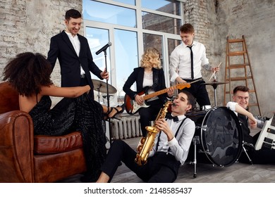 Repetition Of Multi Ethnic Jazz Band In Loft. Bass Guitar Player, Electric Guitar Player, Saxophonist And Drummer At Loft. Jazz Music And Jam Session Concept. Passion For Music And Youth Culture