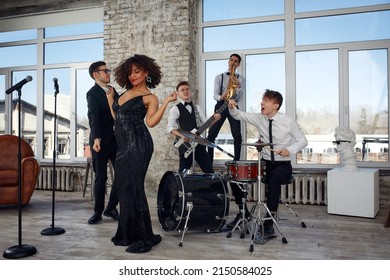 Repetition Of Multi Ethnic Jazz Band In Loft. Bass Guitar Player, Electric Guitar Player, Saxophonist And Drummer At Loft. Jazz Music And Jam Session Concept. Passion For Music And Youth Culture