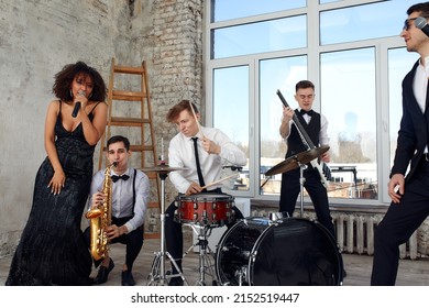 Repetition Of Multi Ethnic Jazz Band In Loft. Bass Guitar Player, Electric Guitar Player, Saxophonist And Drummer At Loft. Jazz Music And Jam Session Concept. Passion For Music And Youth Culture