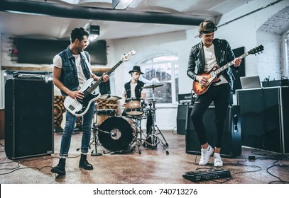 Repetition Of Rock Music Band. Bass Guitar Player, Electric Guitar Player And Drummer Behind The Drum Set. Rehearsal Base