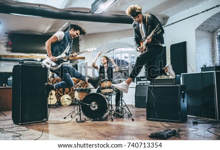 Repetition of rock music band. Bass guitar player, electric guitar player and drummer behind the drum set. Rehearsal base