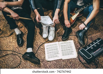 Repetition of rock music band. Cropped image of guitar players and drummer are sitting on the floor at rehearsal base with notes. Top view - Shutterstock ID 742767442
