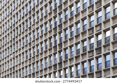A repetitive, geometric grid pattern of a brutalist concrete building facade featuring numerous windows and air conditioning units in Manhattan.