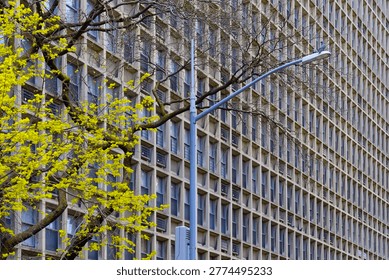 A repetitive, geometric grid pattern of a brutalist concrete building facade featuring numerous windows and air conditioning units in Manhattan.