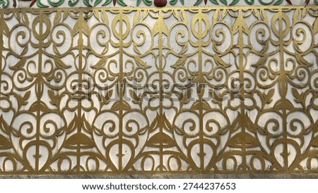 A repetitive and intricate golden scrollwork pattern extends across a white decorative wall, showcasing ornamental details.