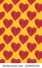 Repetitive pattern made of red glittering hearts. Creative layout on a yellow background.