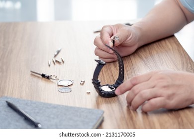 Replace the battery of watch concept: close up hand a man hold pliers to clamp small battery of a watch have a screwdriver, cover, screw and working note on the table 
