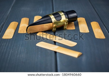 Replacement reeds and saxophone mouthpiece with clamp and golden adjustment screws on gray wooden table
