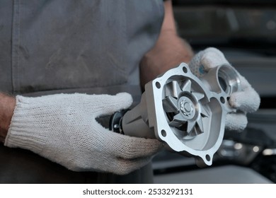 Replacement of the water pump in the car engine. An auto mechanic holds a new water pump, monitors the integrity of the new spare part before installation.